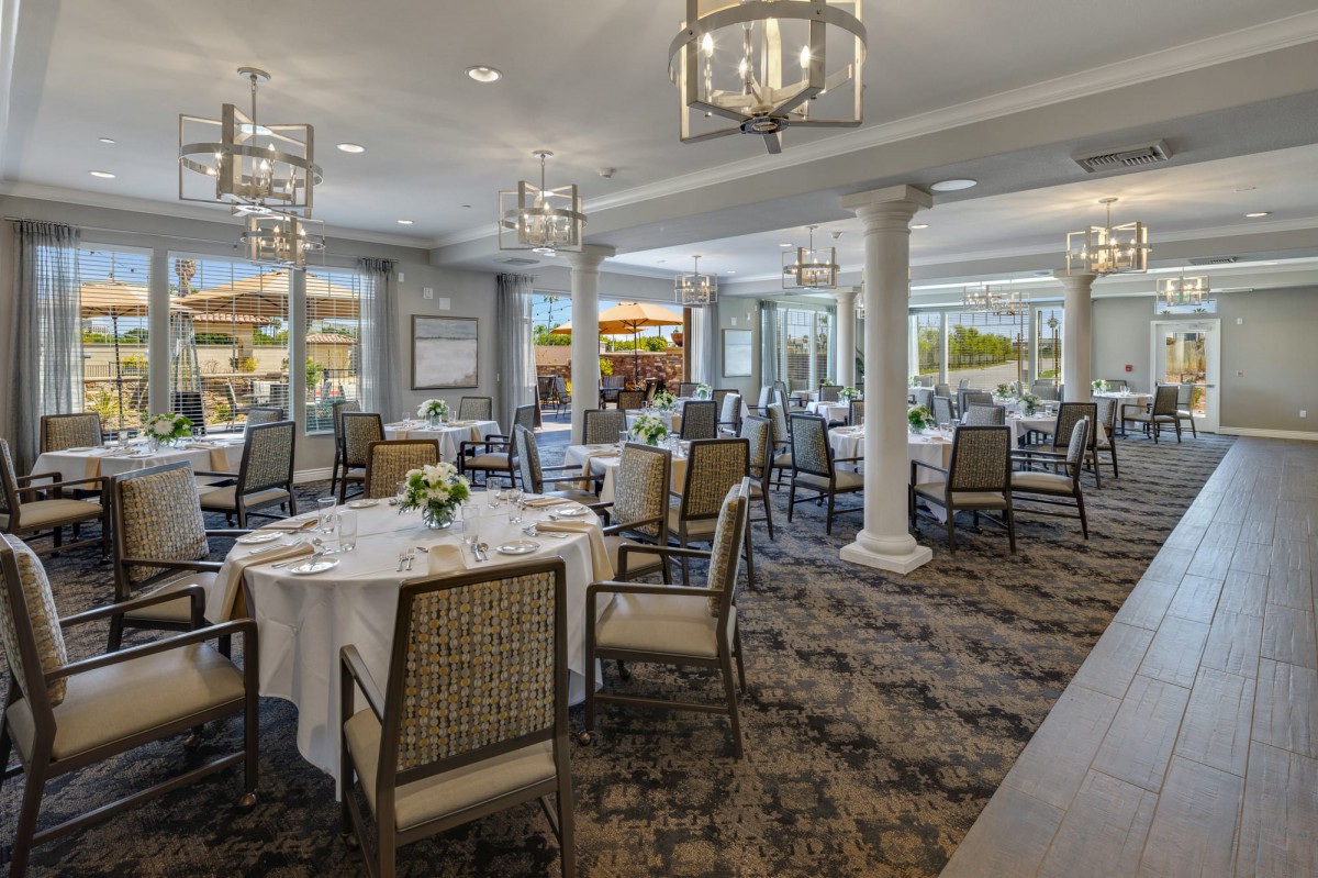 An elegant dining area with beautifully set tables and chandeliers overhead.