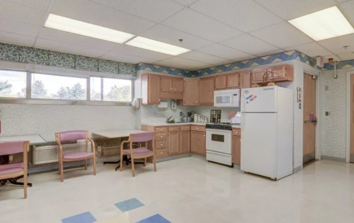 A simple kitchen and dining area with wooden cabinets, a refrigerator, stove, microwave, table, and chairs.