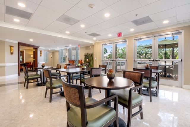 A bright and spacious dining area with multiple tables and chairs, featuring large windows allowing natural light to fill the room.