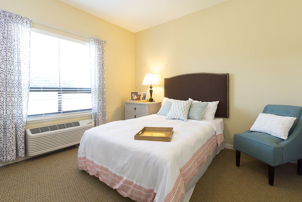 A cozy bedroom with a neatly made bed, a bedside lamp, and a window allowing natural light.