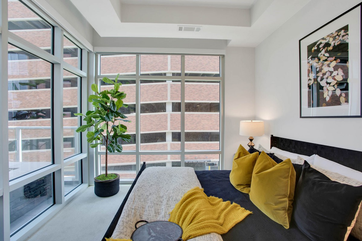 A modern bedroom with large windows, natural light, and yellow accent pillows.