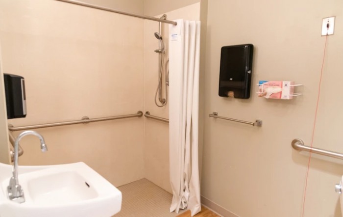 An accessible bathroom featuring a shower with grab bars, a sink, and a hand dryer.