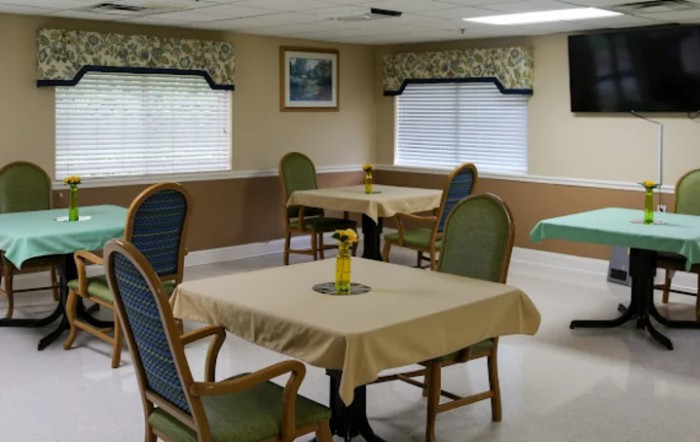 A dining area with neatly arranged tables and chairs, featuring window blinds and decorative elements.