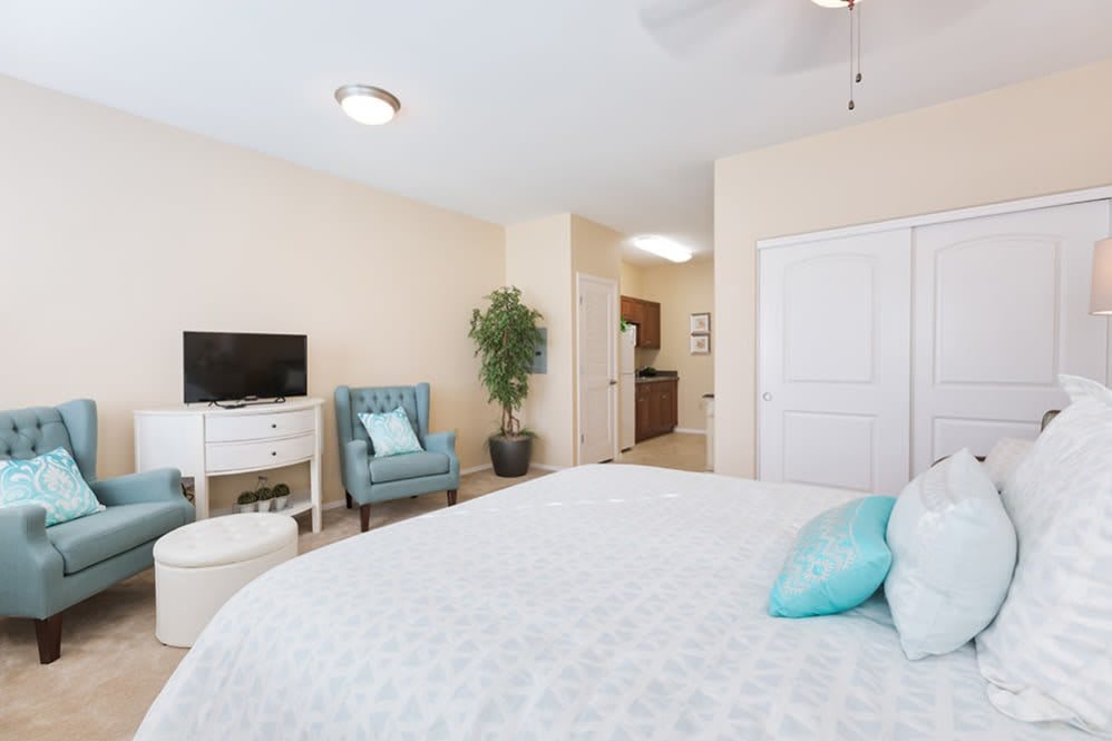 A bright and cozy bedroom with a large bed, a chair, a TV on a stand, and decorative elements.