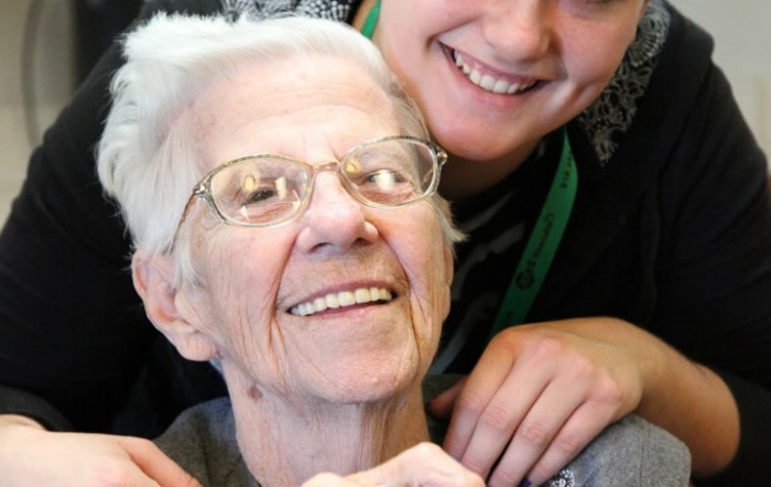 An elderly person smiling warmly while being embraced by another person.
