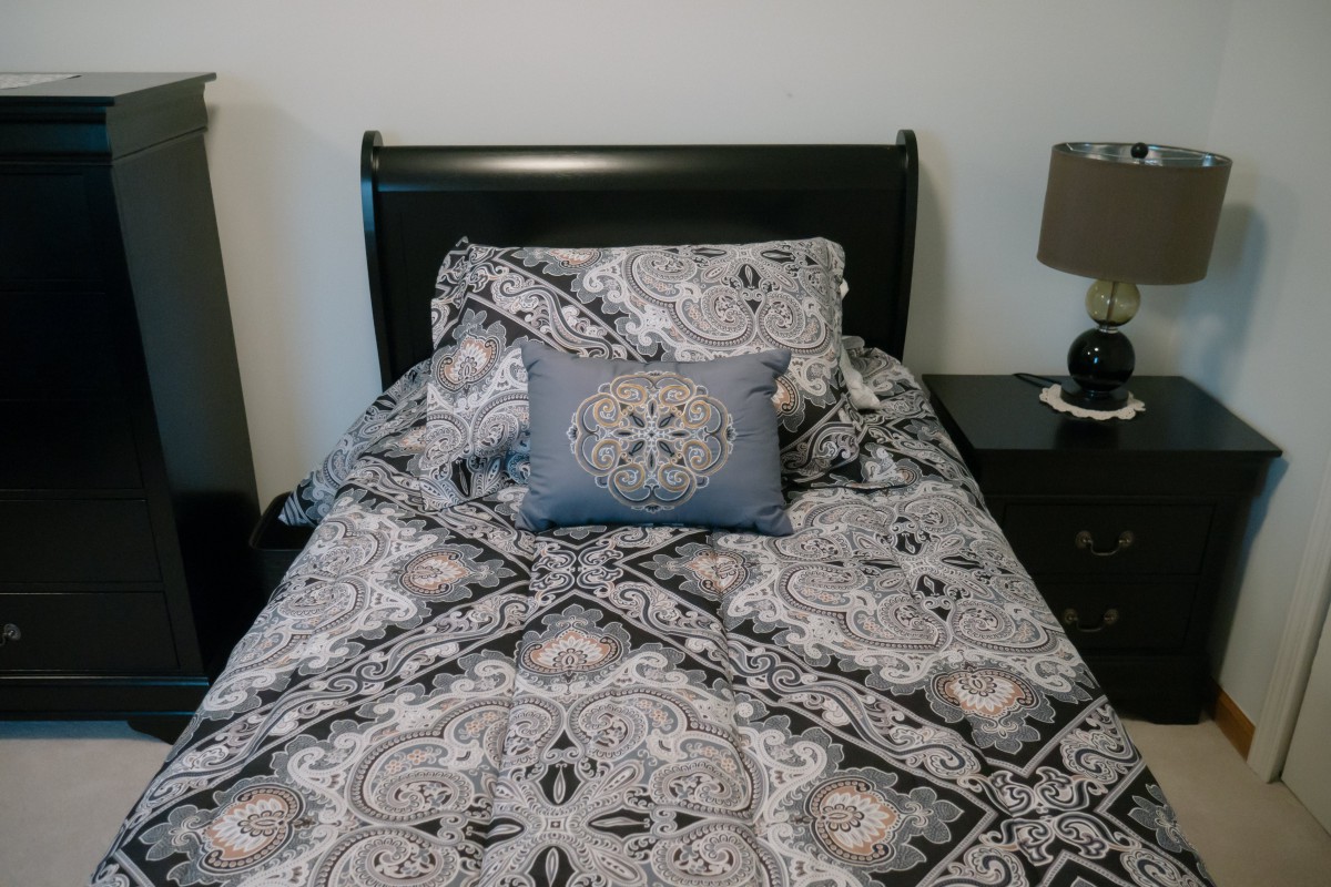 A neatly made bed with patterned bedding and decorative pillows beside a nightstand and lamp.