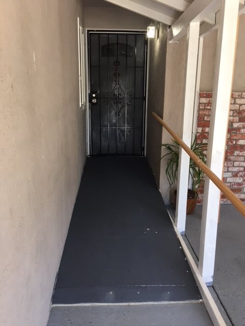 A narrow corridor with a metal door at the end, featuring a handrail and potted plant.
