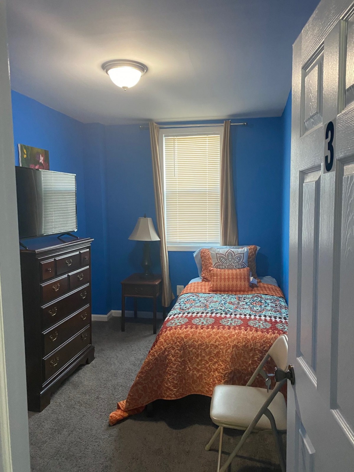 A cozy single bedroom with blue walls and a colorful bedspread.