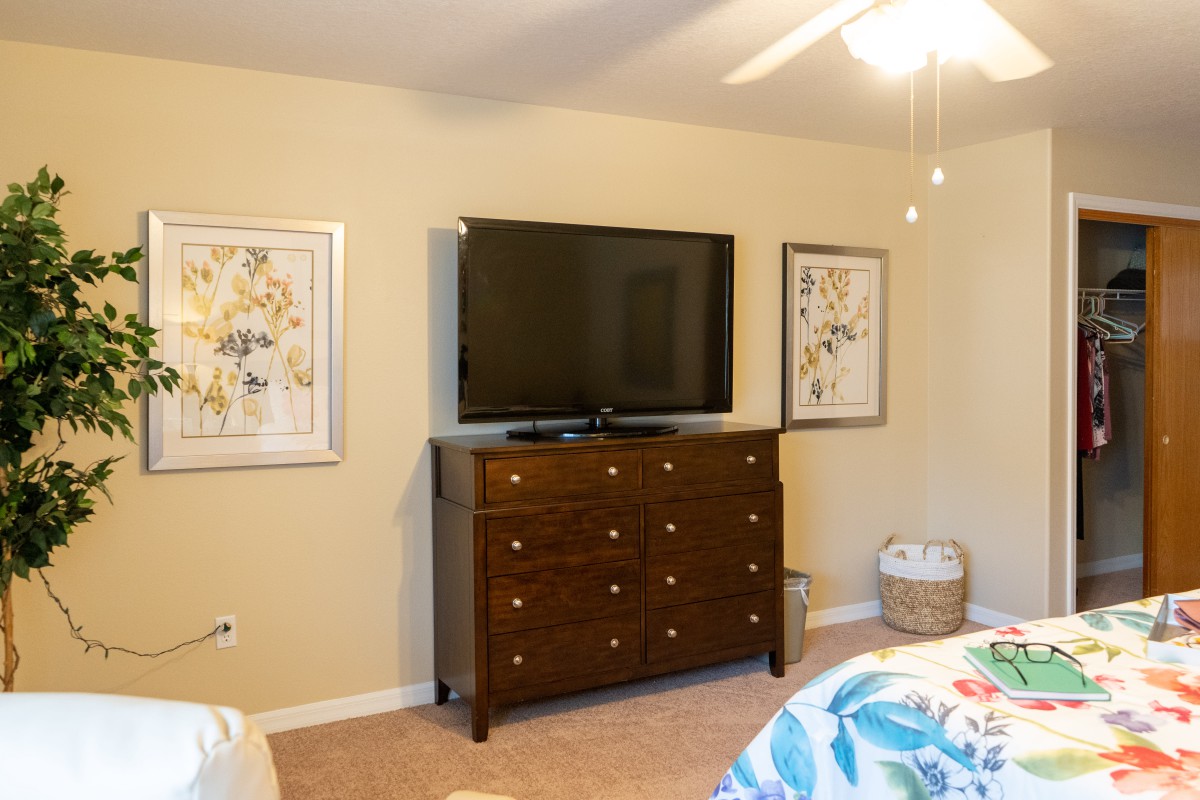 A cozy bedroom with a TV on a dresser and framed artwork on the walls.