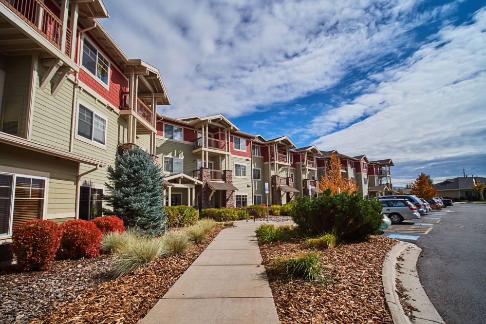 A modern apartment complex with a landscaped walkway under a cloudy sky.