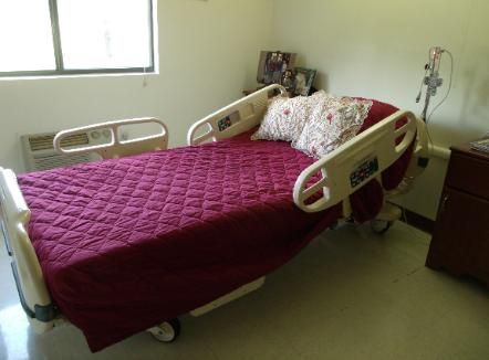 A hospital bed with a red bedspread and pillow in a well-lit room.