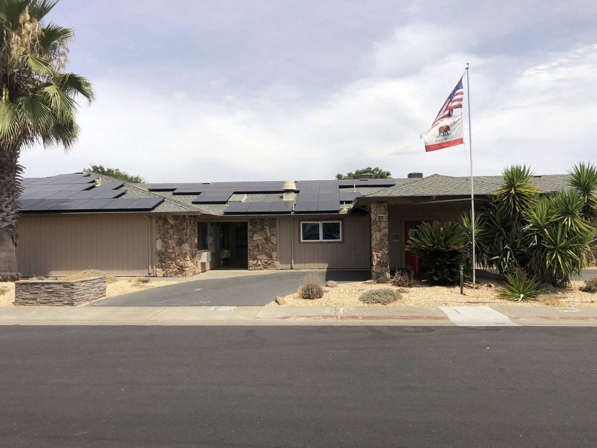 A suburban house with solar panels on the roof and a flag in the front yard.