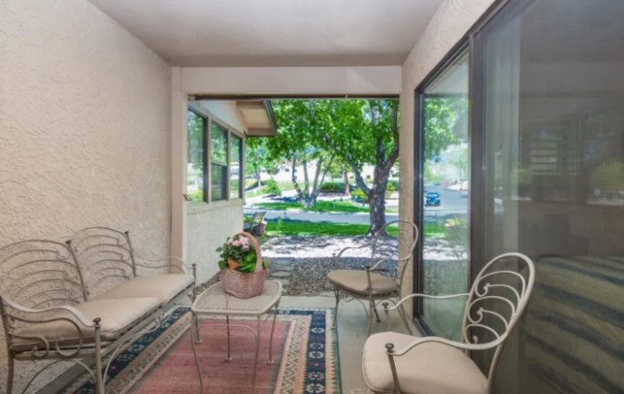 A bright and inviting patio area with modern furniture and large glass windows overlooking a lush, green garden.