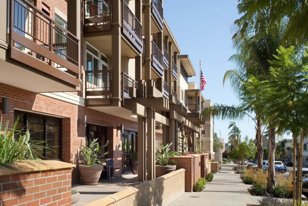 A modern residential street with multi-story buildings featuring balconies and potted plants.