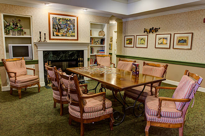 A cozy dining room featuring a wooden table surrounded by upholstered chairs, with artwork on the walls and a fireplace.