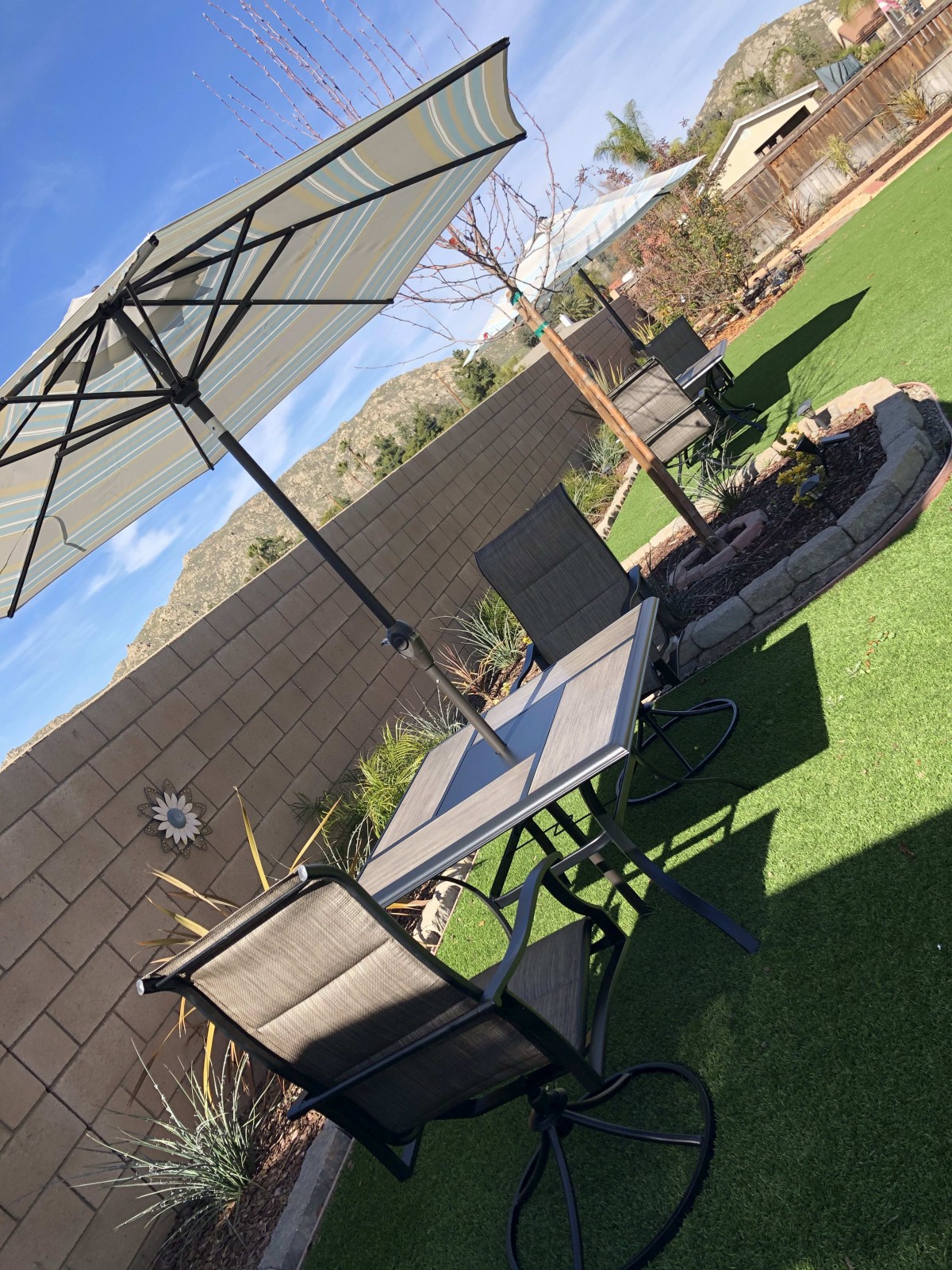 A backyard patio with outdoor furniture and an umbrella on a sunny day.