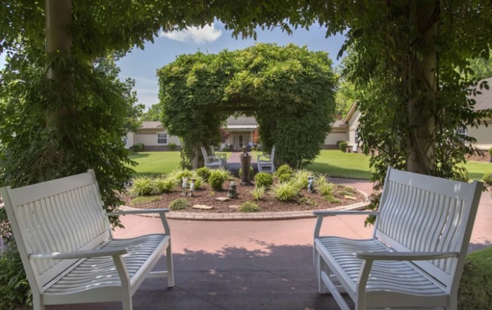 A charming garden view framed by an archway with two white chairs.