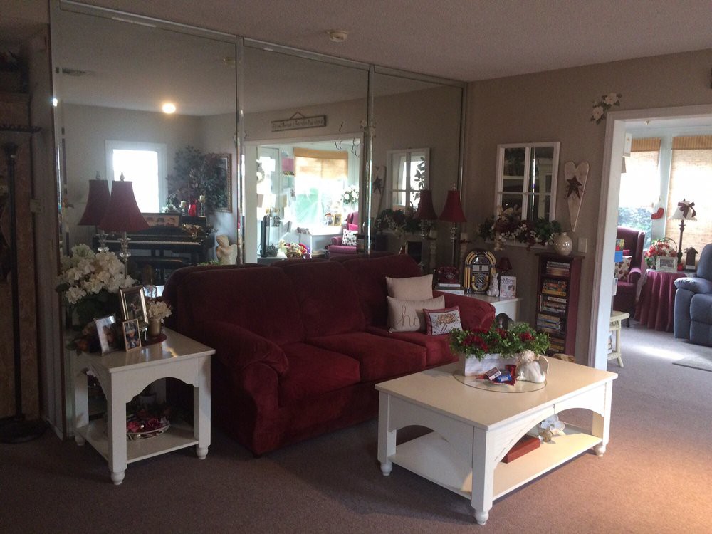 A cozy living room with a red sofa, white coffee and side tables, mirrors on the wall, and various decorations.