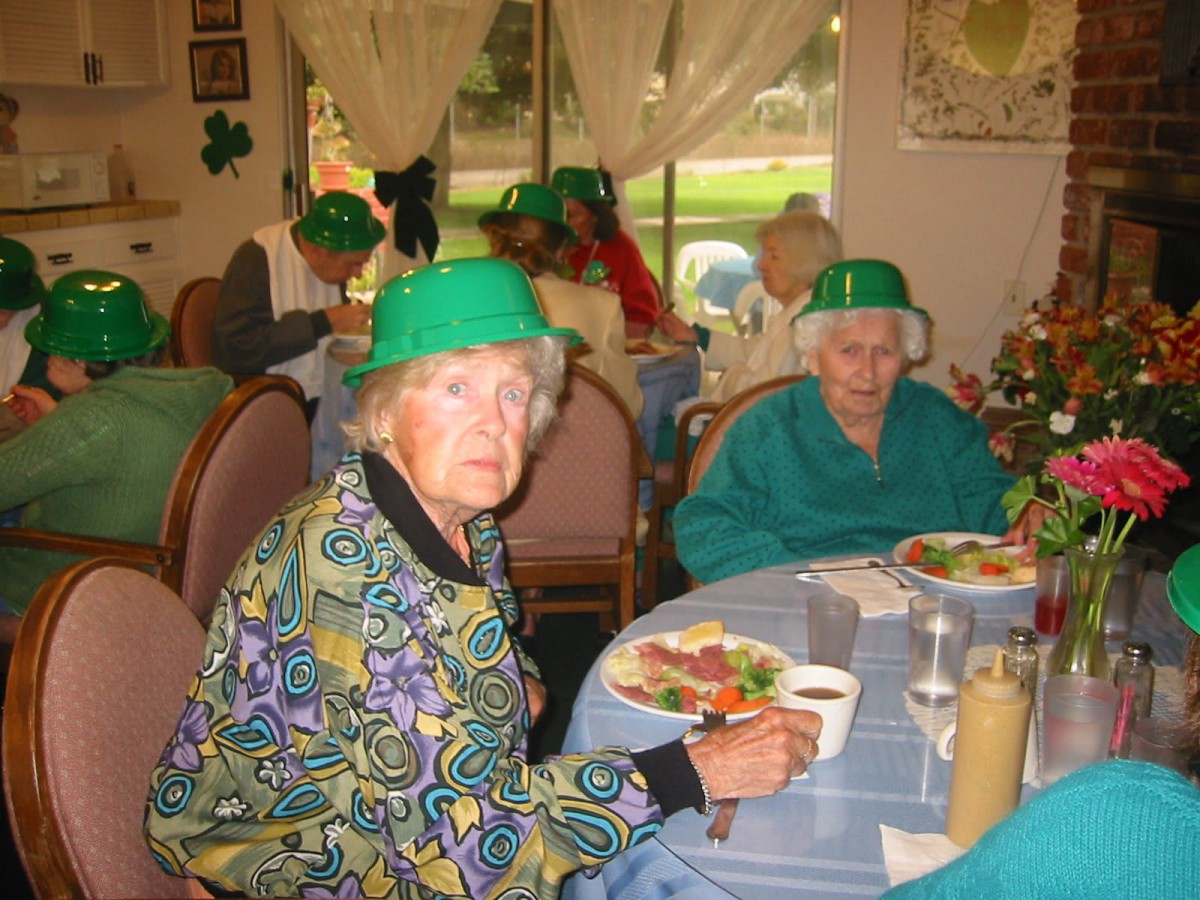 Elderly individuals enjoying a meal while celebrating St. Patrick's Day, wearing festive green hats.