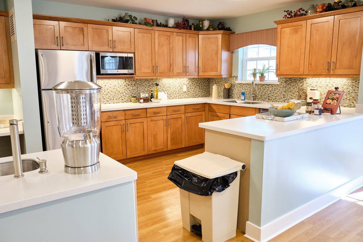A modern kitchen with wooden cabinets, a microwave, and a trash bin on hardwood flooring.