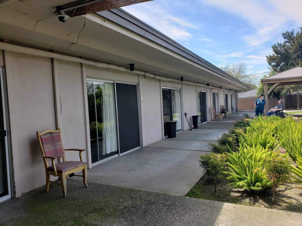 A row of buildings with sliding glass doors opening to a patio area, surrounded by greenery and under a clear blue sky.