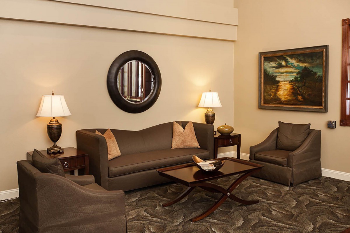 A cozy living room with elegant furniture, including a sofa, armchairs, and a coffee table. The room is adorned with lamps, a circular mirror, and wall art.