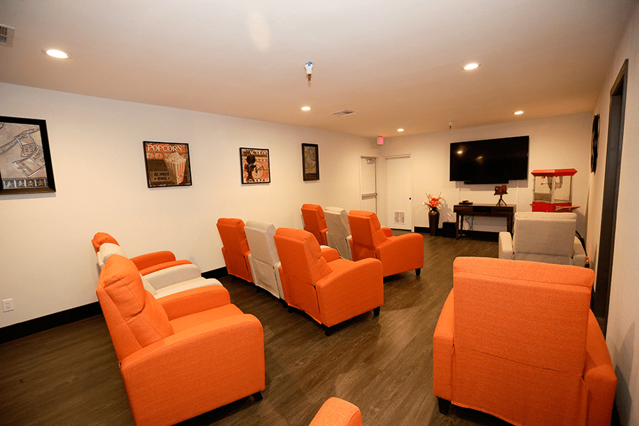A cozy home theater room featuring orange chairs arranged to face a large television on the wall.