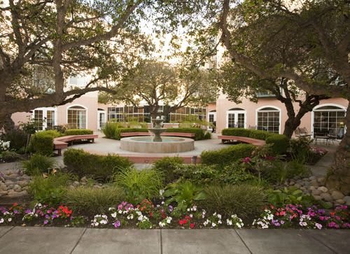 A serene courtyard garden featuring a central fountain surrounded by benches and vibrant flowers.