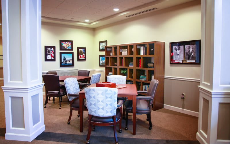 A cozy library corner with tables, chairs, and a bookshelf filled with books.