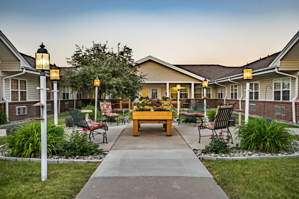 A scenic garden with benches and a pathway leading to a cozy building.