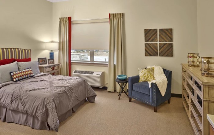 A cozy bedroom featuring a bed, armchair, and window with curtains.