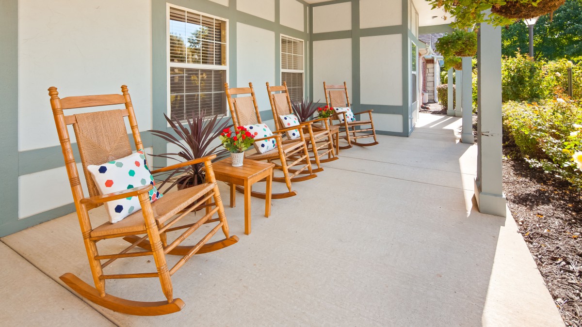A row of wooden rocking chairs with cushions on a spacious patio, perfect for relaxation.