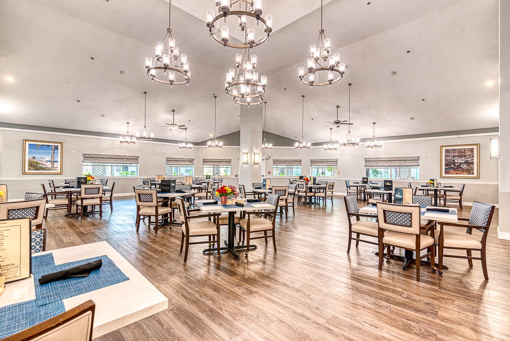 A spacious dining room with elegant chandeliers, wooden flooring, and neatly arranged tables and chairs.