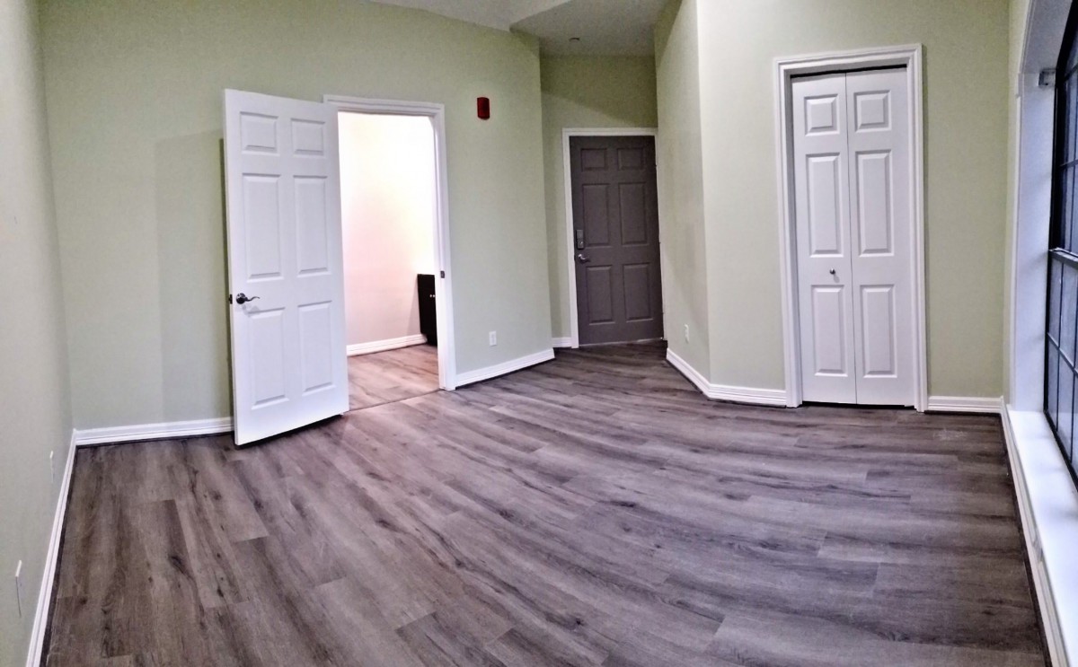 An unfurnished room with hardwood floors, light-colored walls, and several doors.