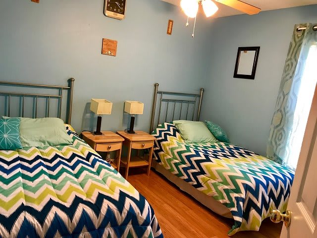 A cozy bedroom with twin beds featuring colorful chevron-patterned bedding, adorned with lamps and a ceiling fan.