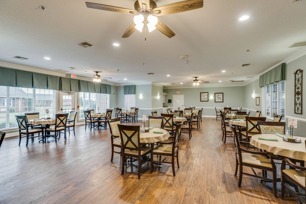 A spacious dining area with wooden floors, multiple tables and chairs, and ceiling fans.