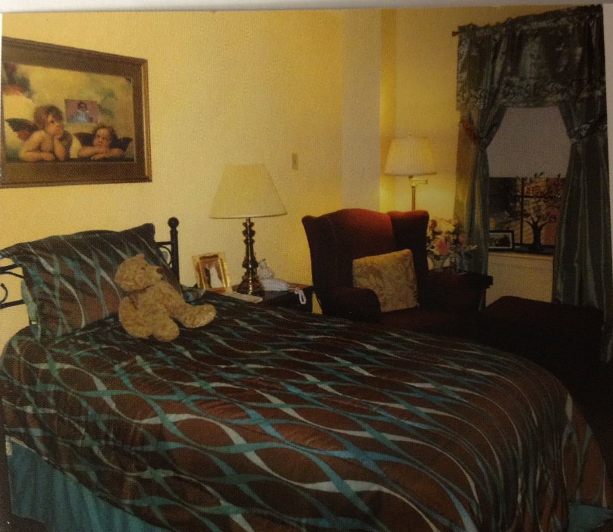 A cozy bedroom with a well-decorated bed, featuring patterned bedding, lamps, armchair, and curtain accents.
