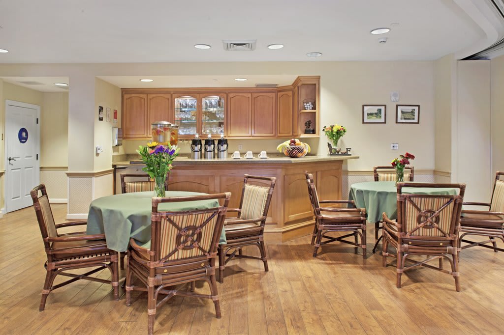 A cozy dining area with several tables and chairs, featuring a kitchenette in the background.