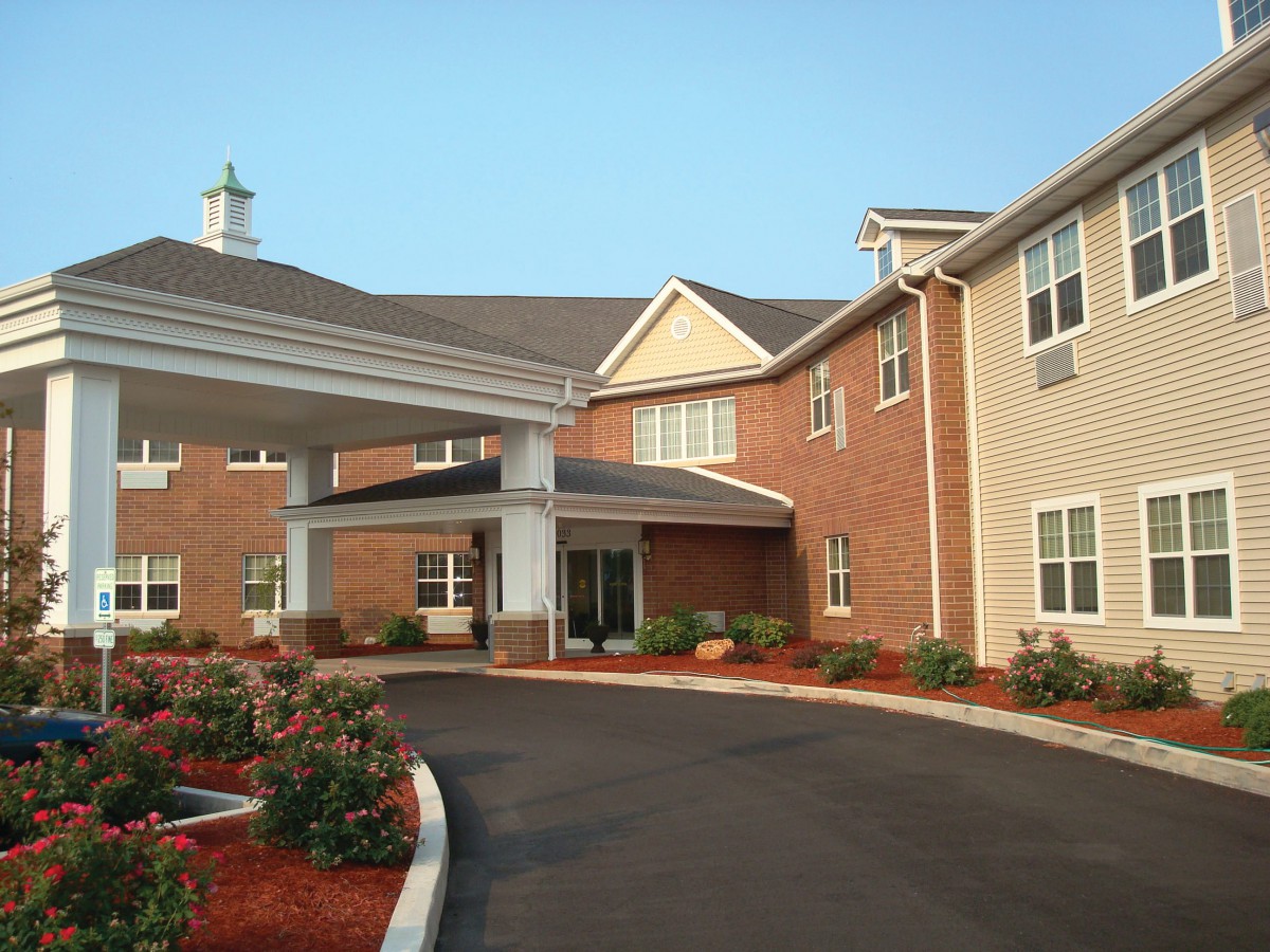 A modern residential building with a covered entrance and landscaped driveway.