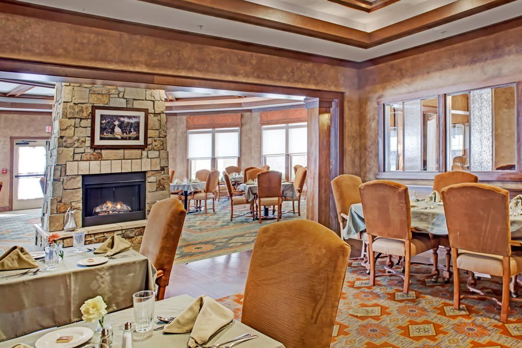 A cozy and elegantly decorated dining room with warm tones, featuring a fireplace and well-arranged tables and chairs.