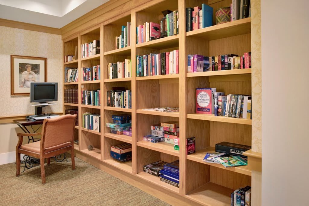 A cozy study room featuring a large wooden bookshelf filled with books and board games.
