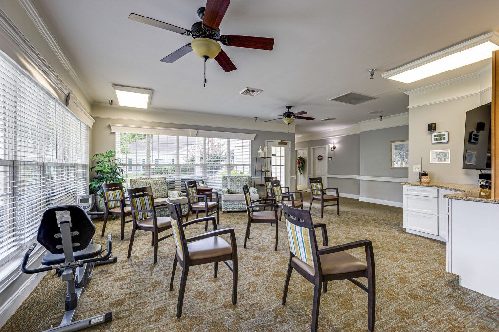 A spacious meeting room with multiple chairs arranged in a circle, featuring large windows and ceiling fans.