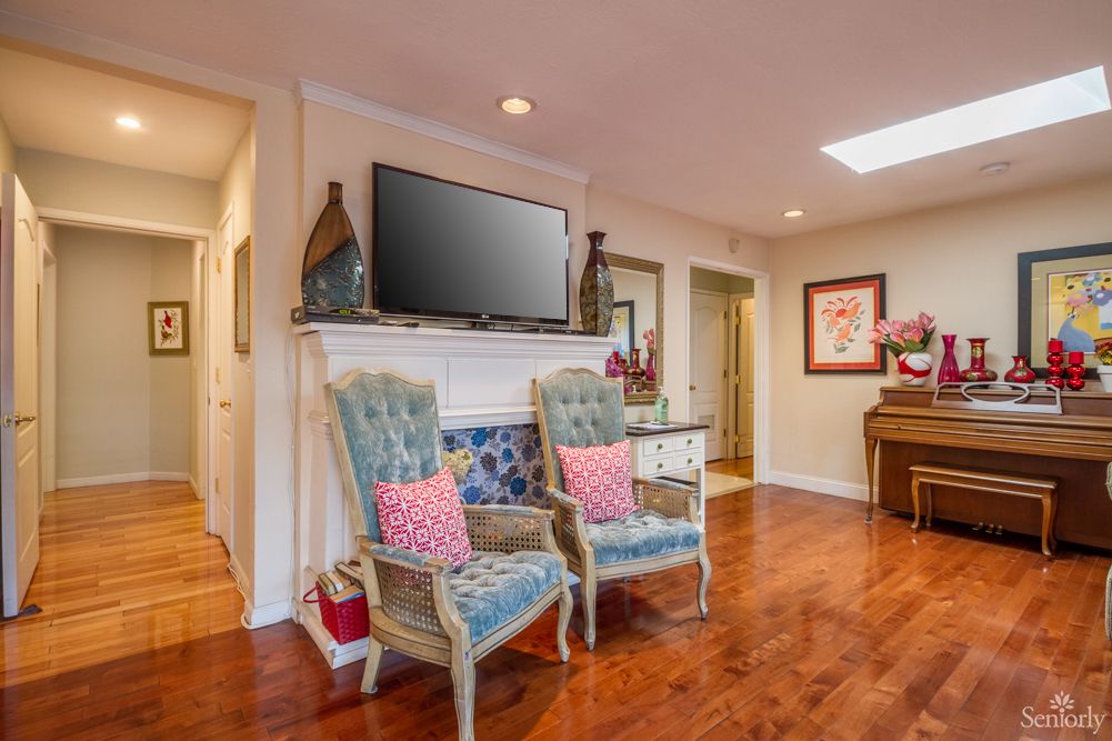 A cozy living room with comfortable chairs, a television mounted above the fireplace, and elegant decor.
