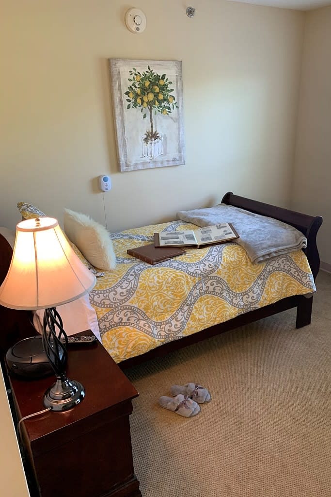 A cozy bedroom with a neatly arranged bed, bedside lamp, and artwork on the wall.