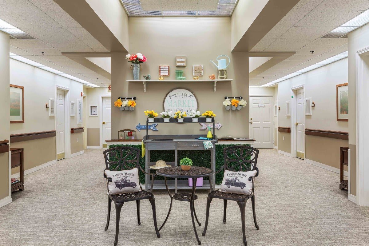 A hallway interior with a decorative setup featuring chairs, shelves adorned with flowers, and a centered mirror.