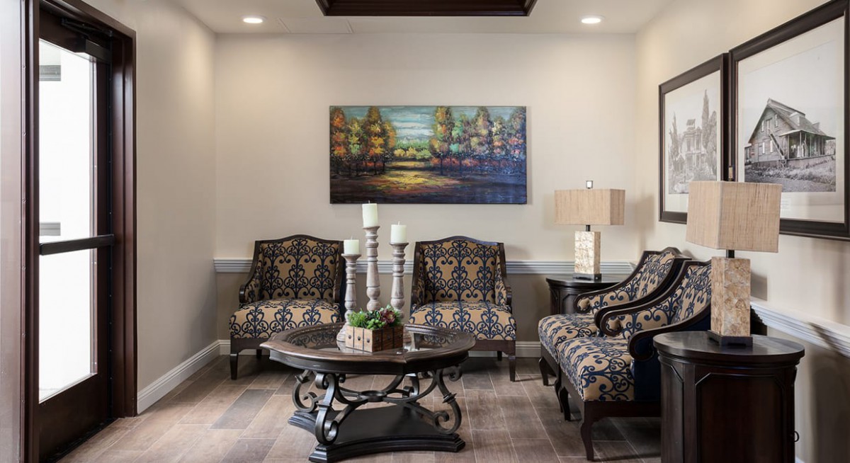 A cozy living room with patterned chairs, a central coffee table, and a colorful painting on the wall.