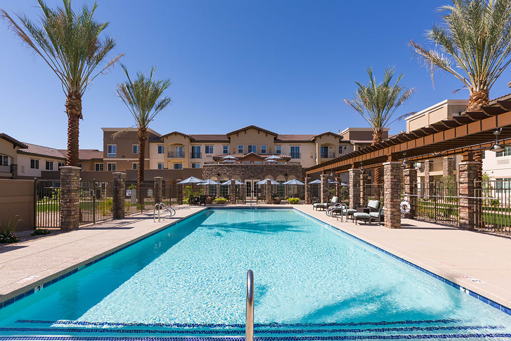 A luxurious resort with an inviting swimming pool surrounded by palm trees and clear blue skies.