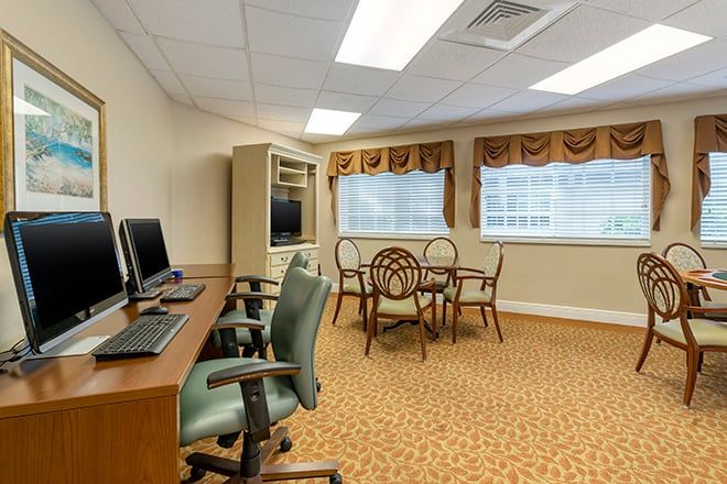 A well-lit office space featuring computers on desks and a round table with chairs near windows.