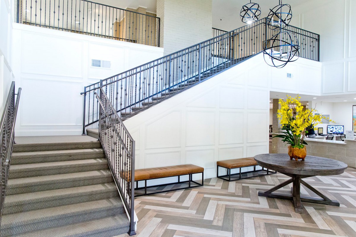 A modern interior with a staircase featuring metal railings, wooden benches, and a decorative table.