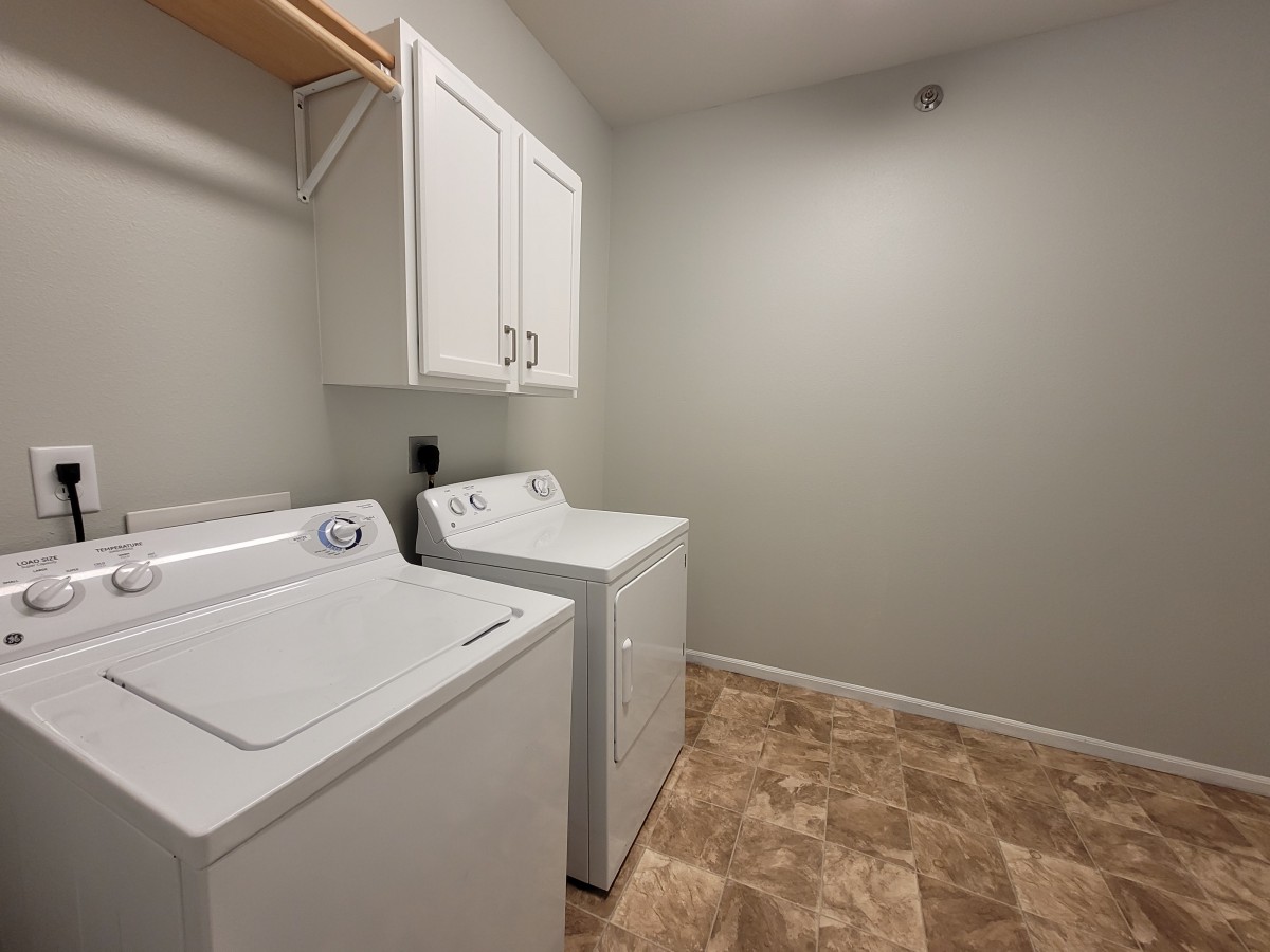 A clean laundry room featuring a washer and dryer set with overhead cabinets.